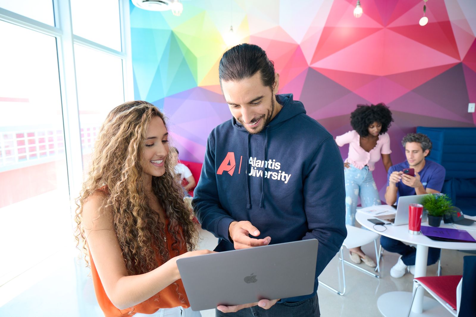 Two students chat over a laptop; one wears an Atlantis University hoodie