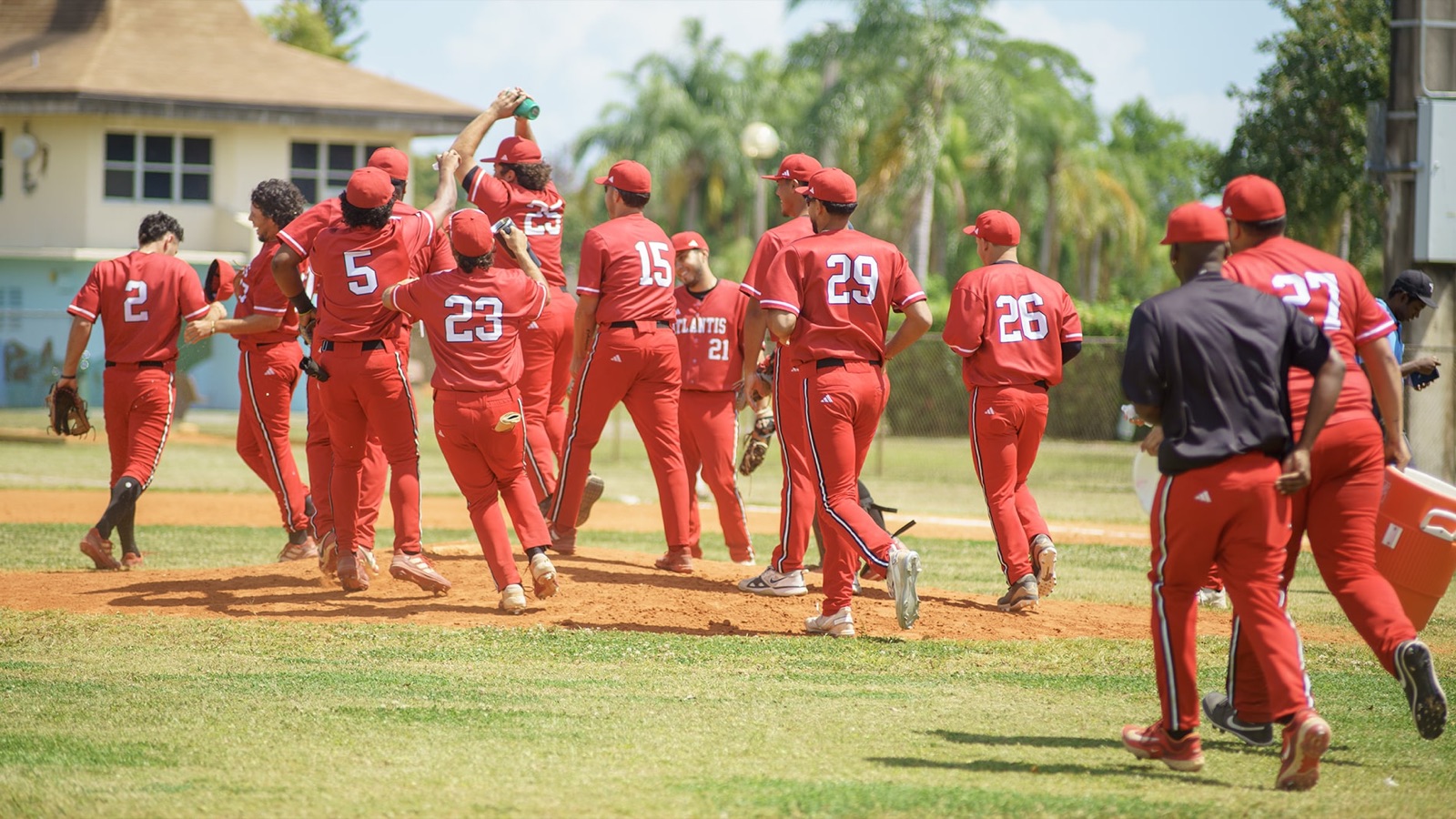 Atlantis University baseball players in red uniforms celebrate on the field after a win