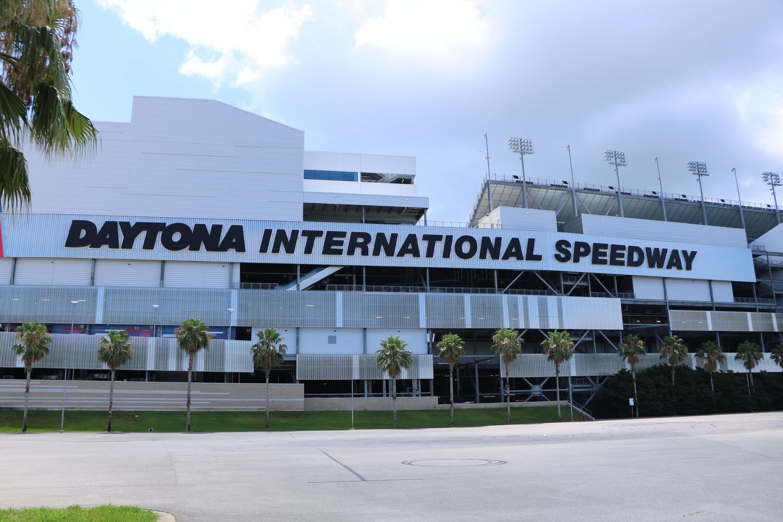Front of the Daytona International Speedway, home of the Daytona 500, with palm trees in front and the name in black letters