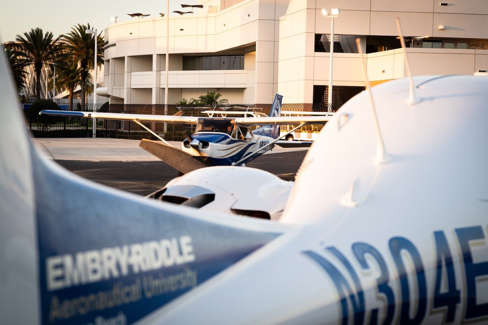 Embry-Riddle-branded Cessna training aircraft on the Daytona Beach campus flight line at sunset, with a campus building and palm trees behind