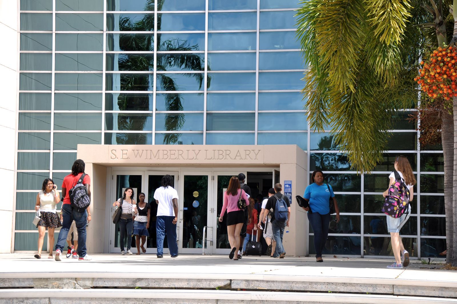 Students walking into the S.E. Wimberly Library, the glass-fronted library with palm trees on FAU's Boca Raton campus