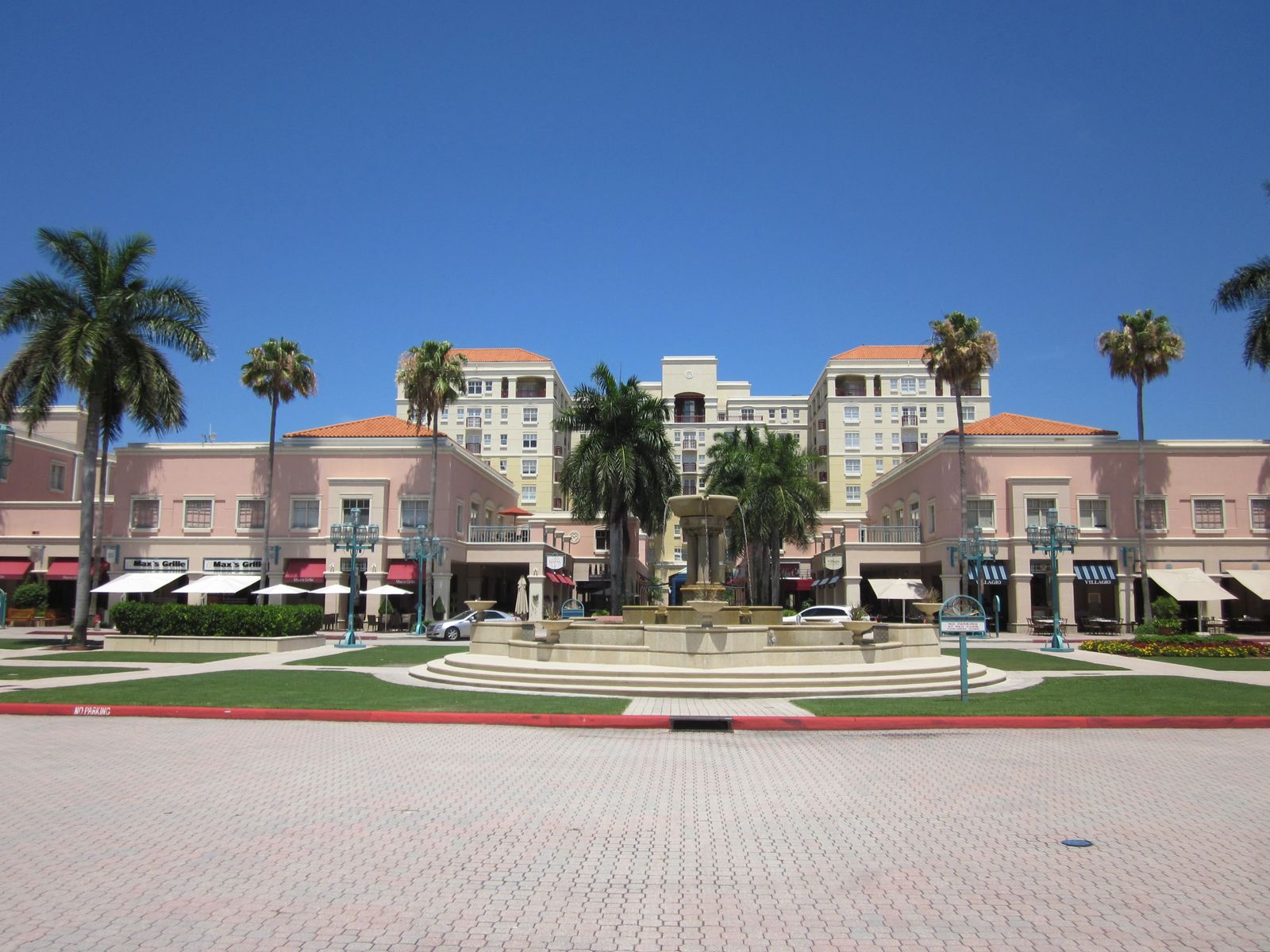 The central plaza of Mizner Park in Boca Raton, with its fountain, pink facades and royal palms on a sunny day