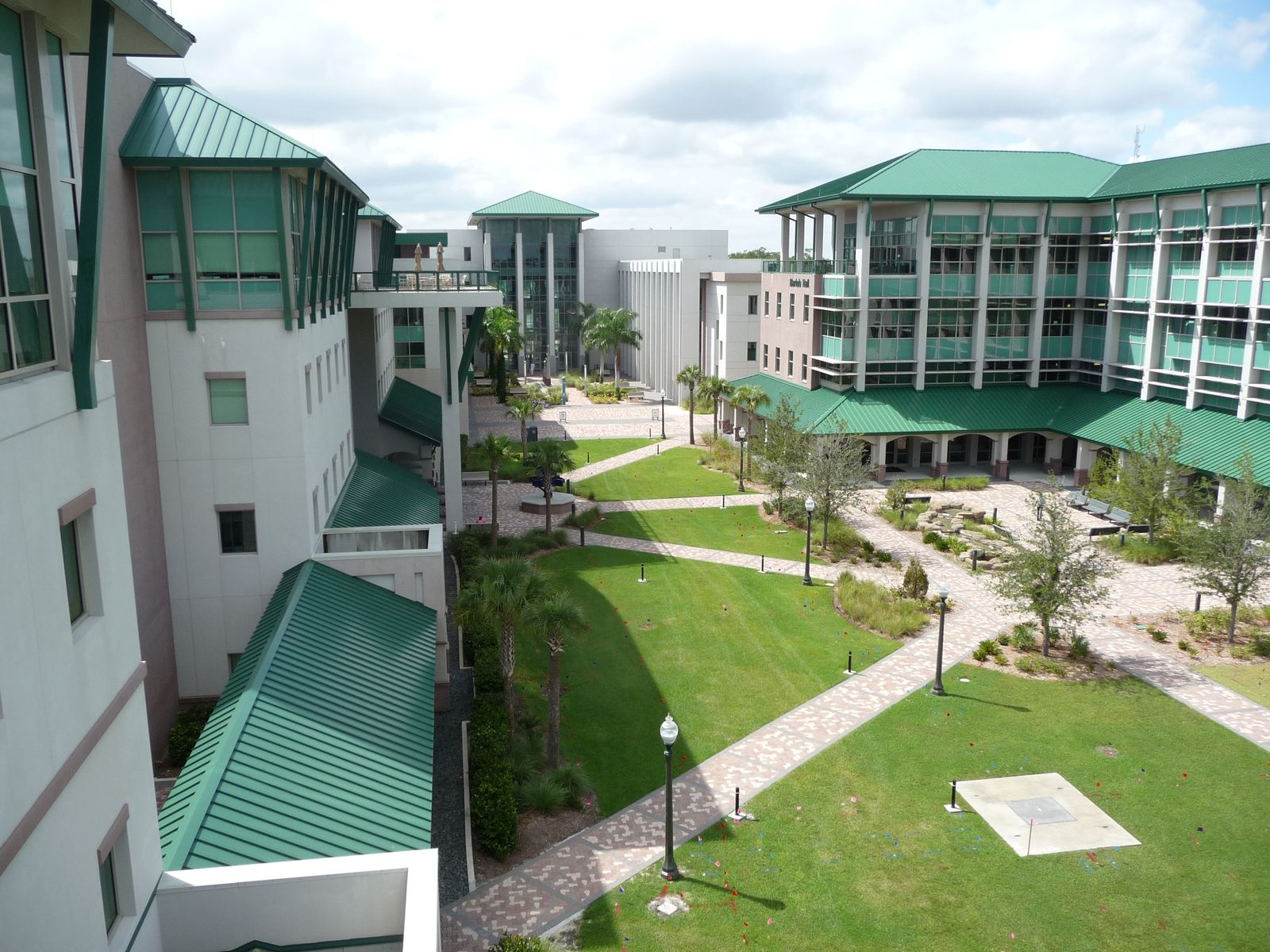View from a balcony over the lawned courtyard of FGCU's Academic Core, with paths, palms and green-roofed buildings around it