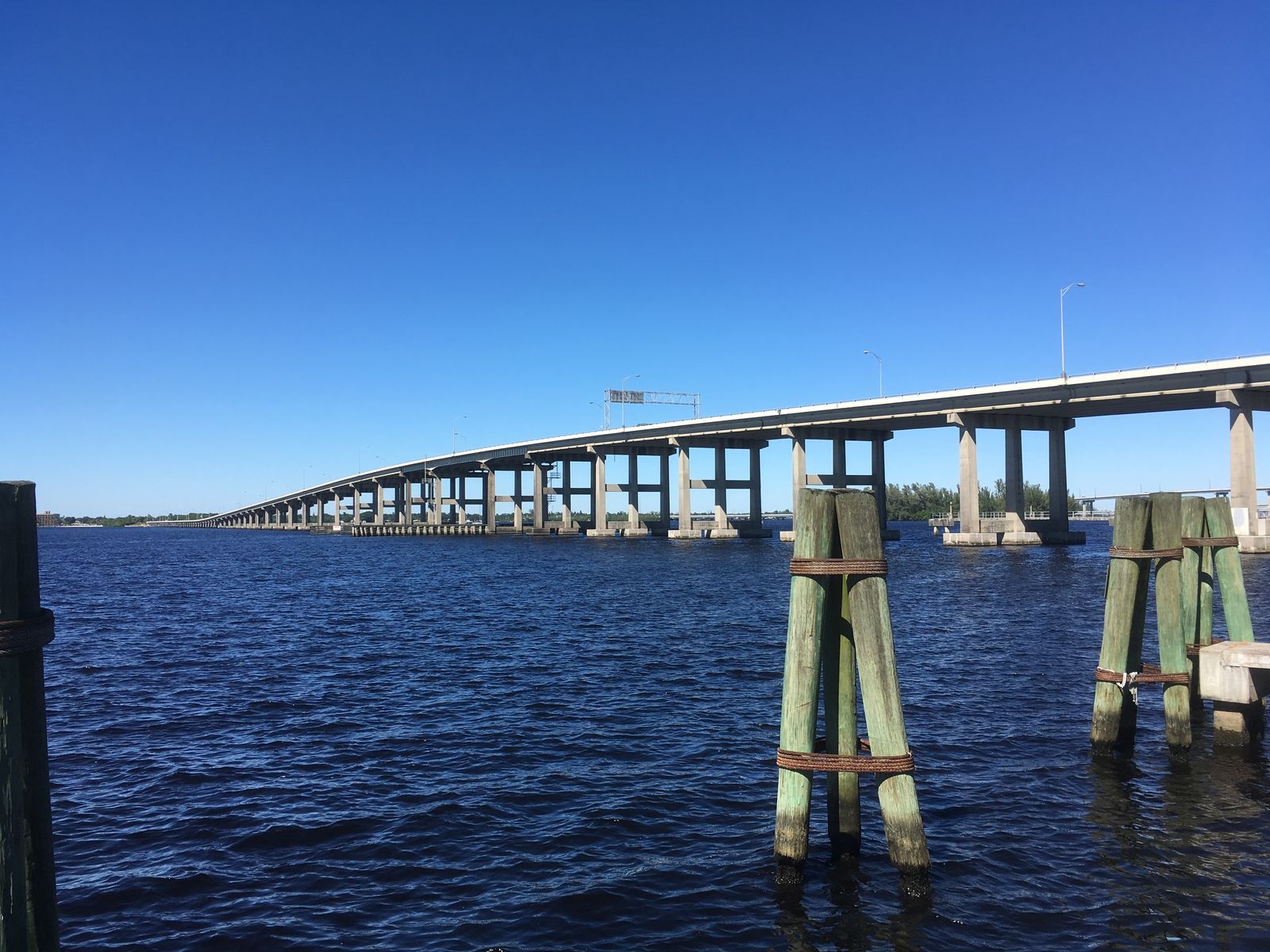 The Caloosahatchee Bridge (US 41) crossing the Caloosahatchee River in Fort Myers, with wooden pilings in the foreground and blue sky