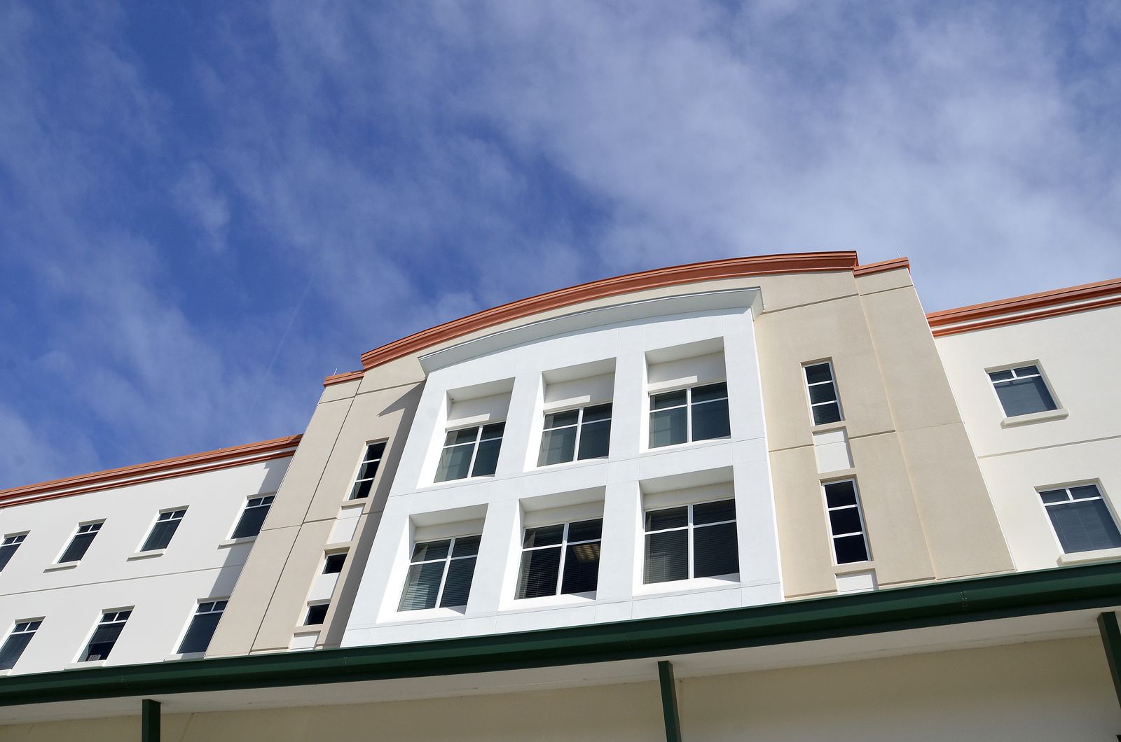 Facade of a four-storey FGCU residence hall in beige and white, seen from below against a blue sky