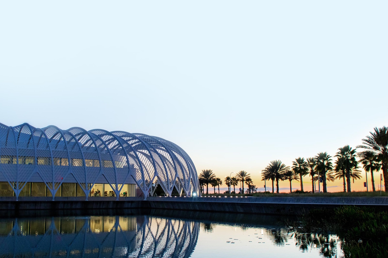 Florida Poly's Innovation, Science and Technology (IST) Building at dusk, with palm trees reflected in the campus lake