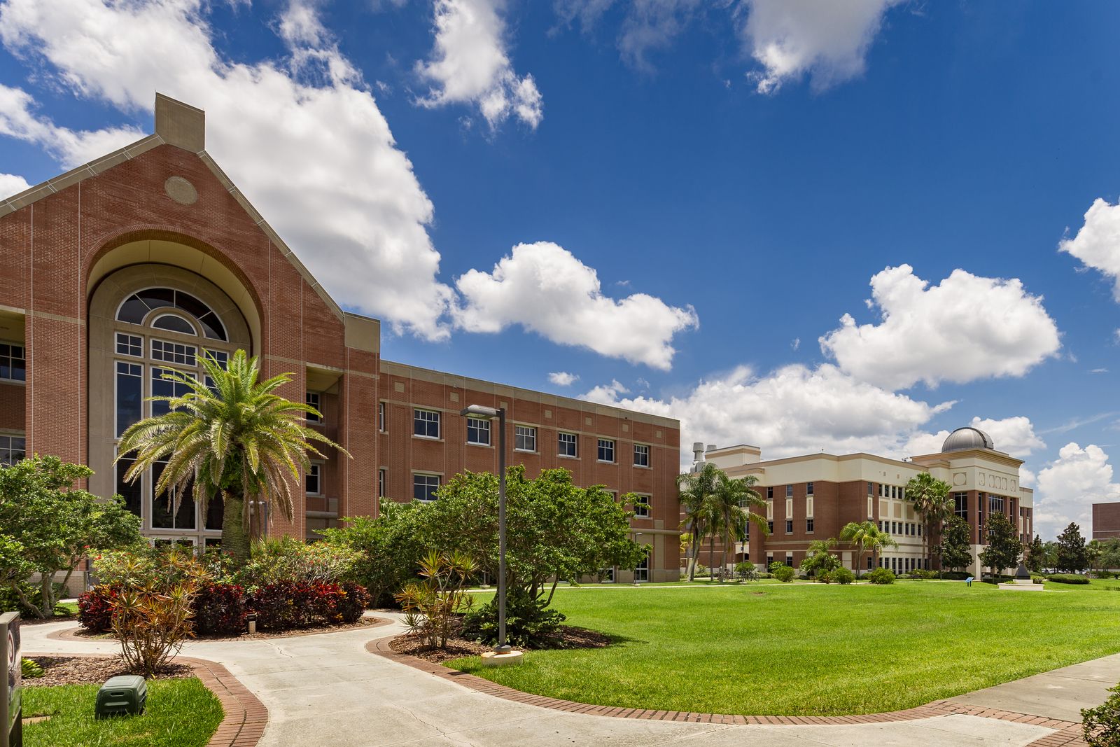 Olin Quad at Florida Tech: brick buildings, palm trees and lawn under a blue sky with clouds