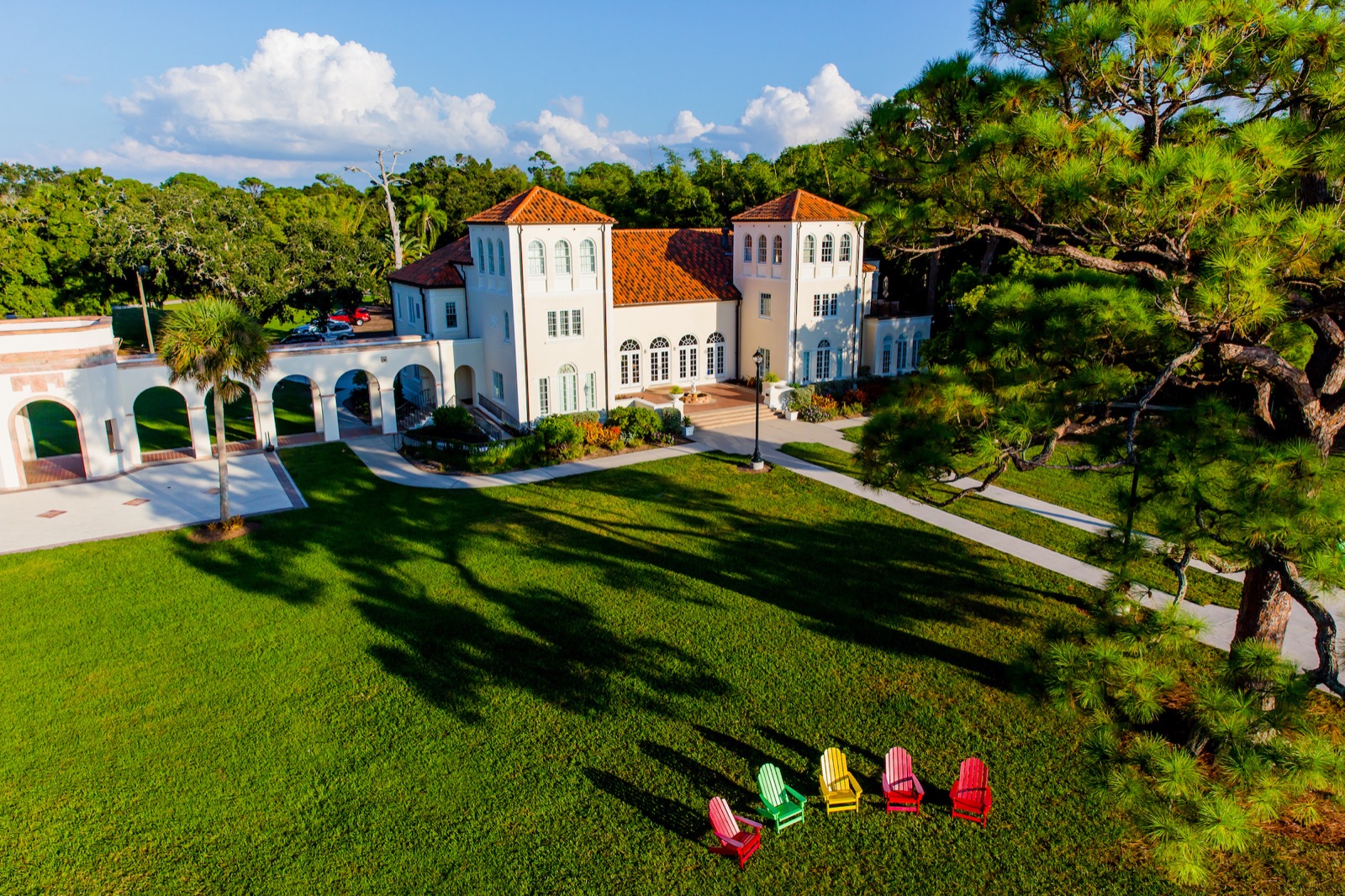 Historic Mediterranean-style building on New College of Florida's Bayfront campus seen from above, with the lawn, colourful chairs and Sarasota Bay in the background