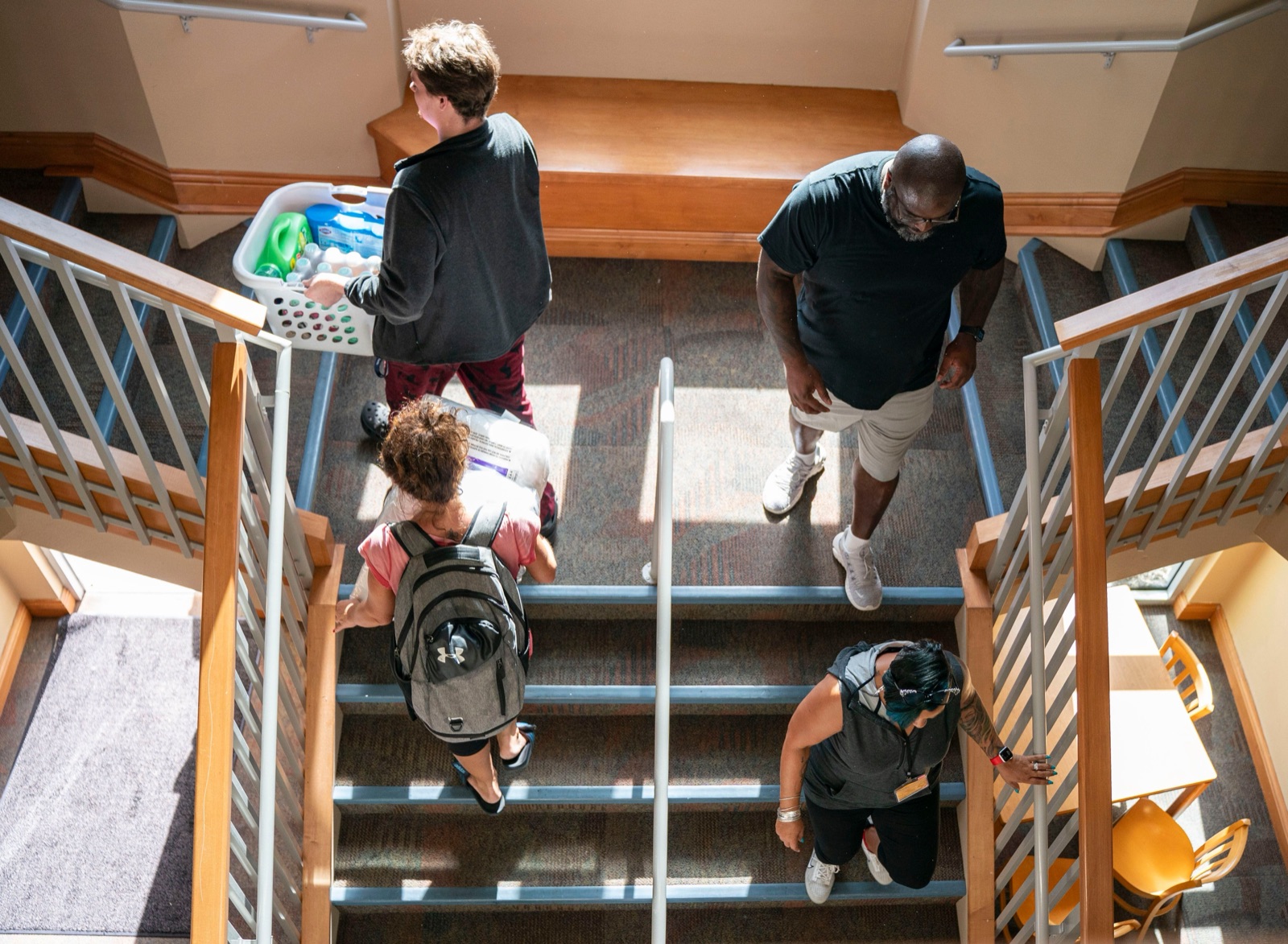 Students going up and down the indoor stairs of a New College of Florida residence hall on move-in day, one of them carrying a laundry basket