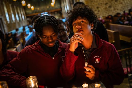 Dois alunos de blusa grená da Church Farm School em um culto na capela à luz de velas