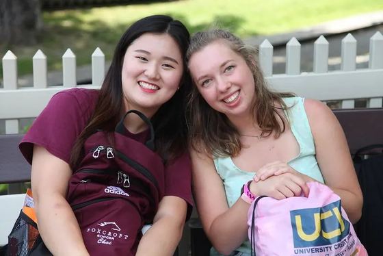 Duas alunas internas sorrindo sentadas ao ar livre, uma com camiseta do futebol da Foxcroft