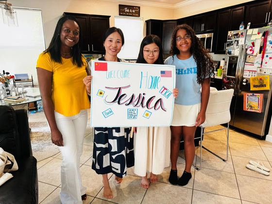 Família anfitriã recebendo um aluno internacional com um cartaz 'Welcome Home' feito à mão na cozinha