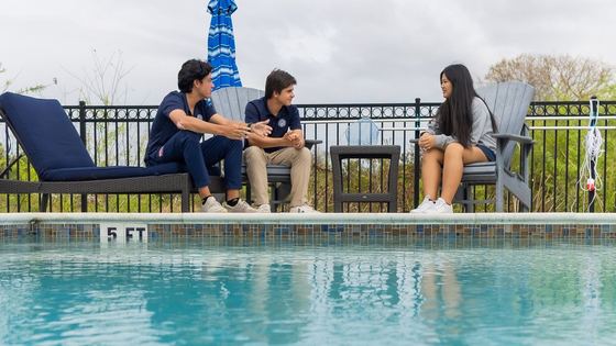 Três alunos internos de uniforme conversando em espreguiçadeiras ao lado da piscina da vila residencial