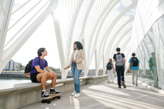 Estudantes conversam e caminham sob os arcos brancos da pérgola do prédio IST da Florida Poly