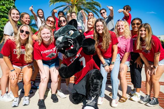 Estudantes com camisetas vermelhas da Florida Tech se divertem ao lado do mascote Pete the Panther