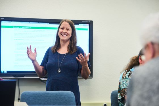 Professora de inglês dando aula diante de uma tela interativa em uma sala de aula modelo da UWF. com estudantes em primeiro plano