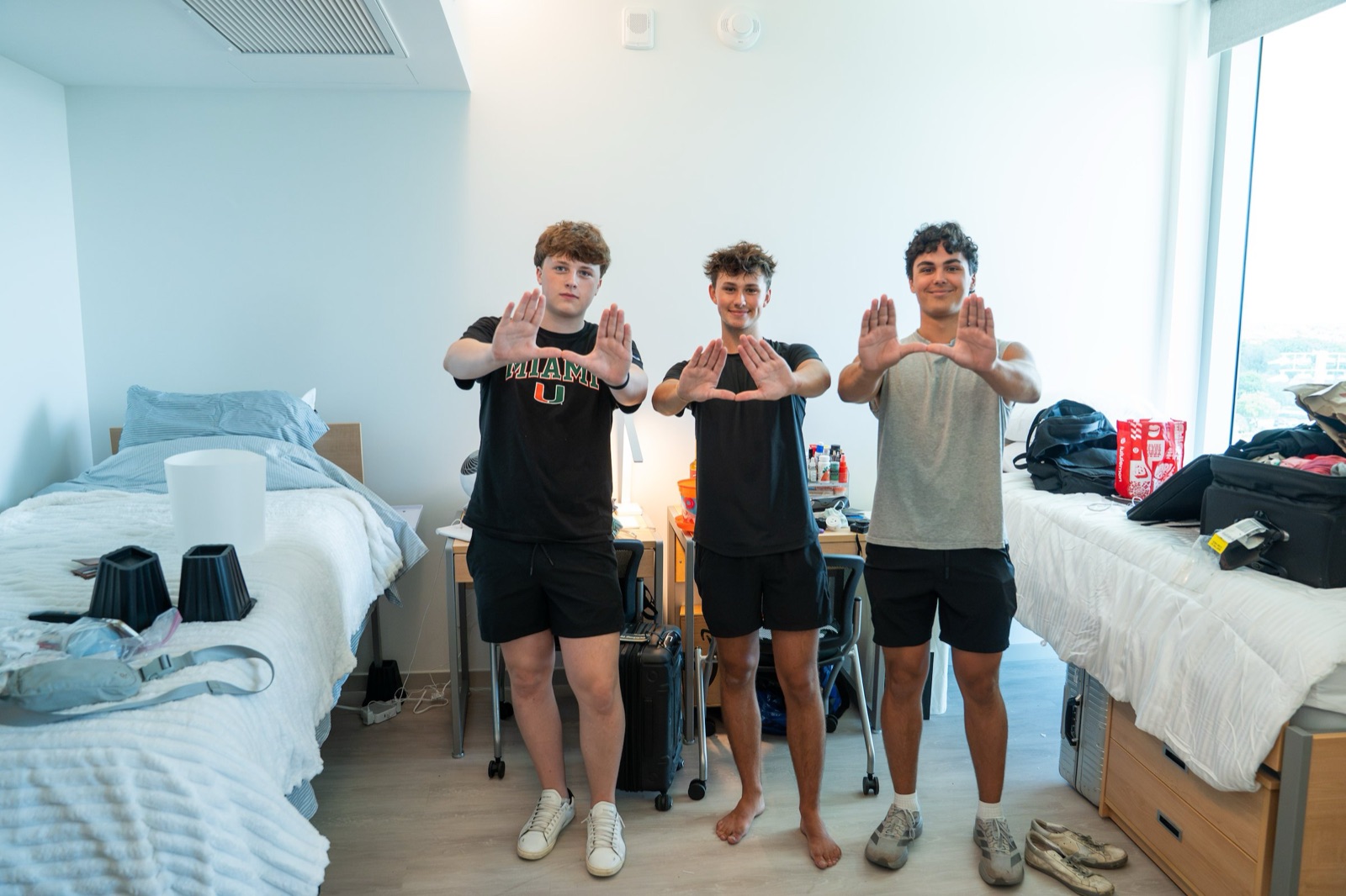 Three first-year students throwing up the U in their newly set-up room in a University of Miami residence hall