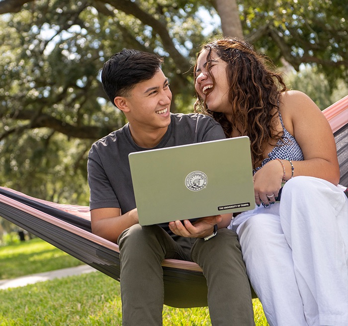 Dois estudantes conversando em uma rede sob os carvalhos do Plant Park, com um notebook no colo