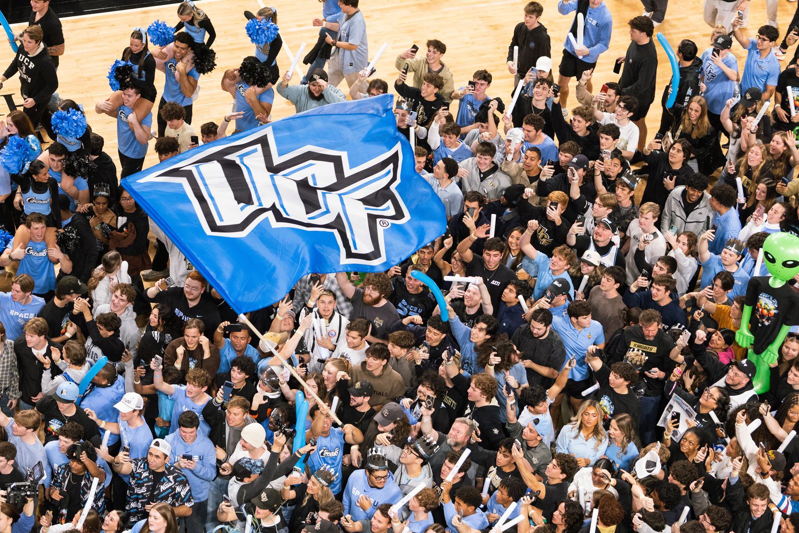 Crowd of UCF students dressed in light blue waving a UCF flag and thunder sticks at the Space Game