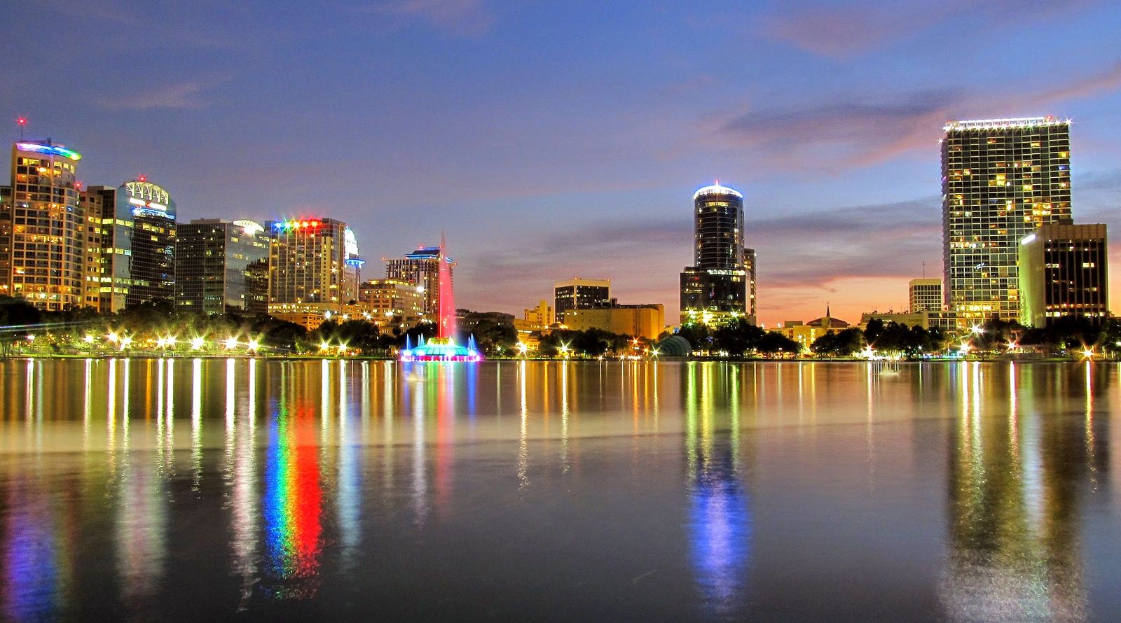 Downtown Orlando skyline at dusk reflected in Lake Eola, with the fountain lit in colours