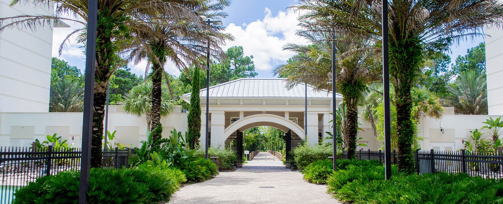 Entrance to Osprey Fountains, a UNF residence hall, with palm trees and archway