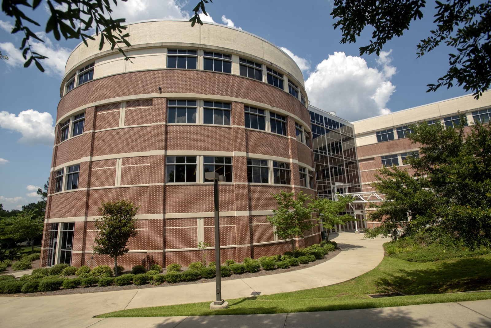 Brick-and-glass building of UWF's Hal Marcus College of Science and Engineering (Building 4) under a blue sky with clouds