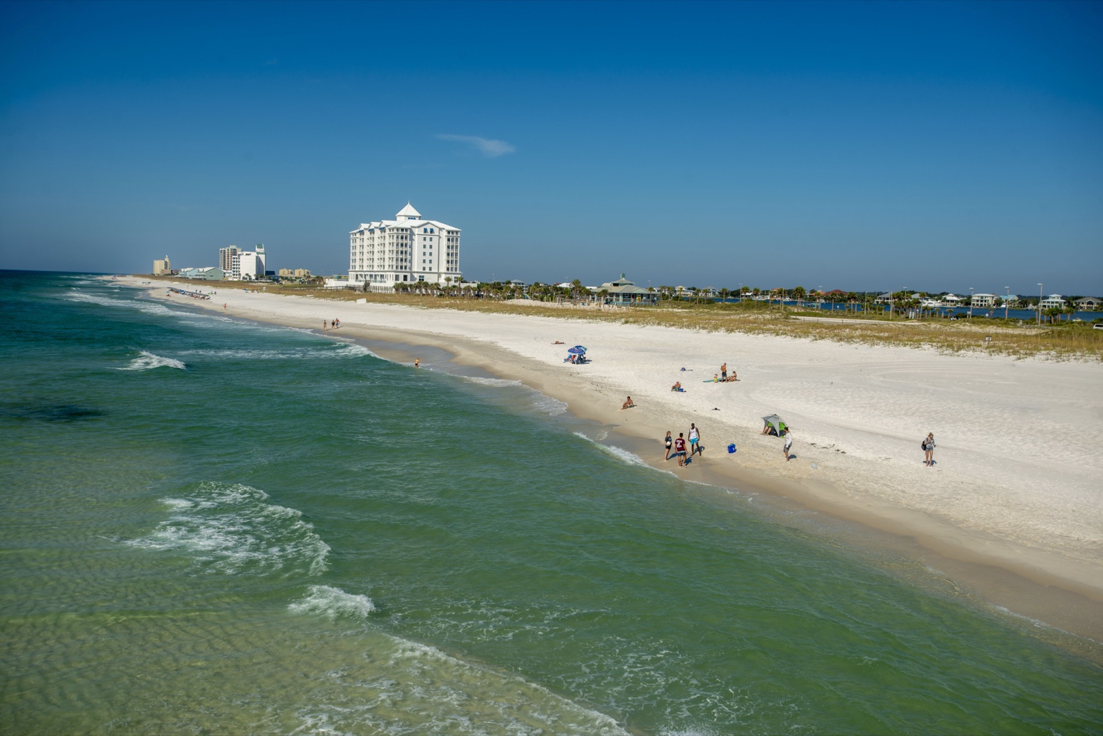 White sand and emerald water at Pensacola Beach on the Gulf of Mexico, with beachgoers and buildings in the distance