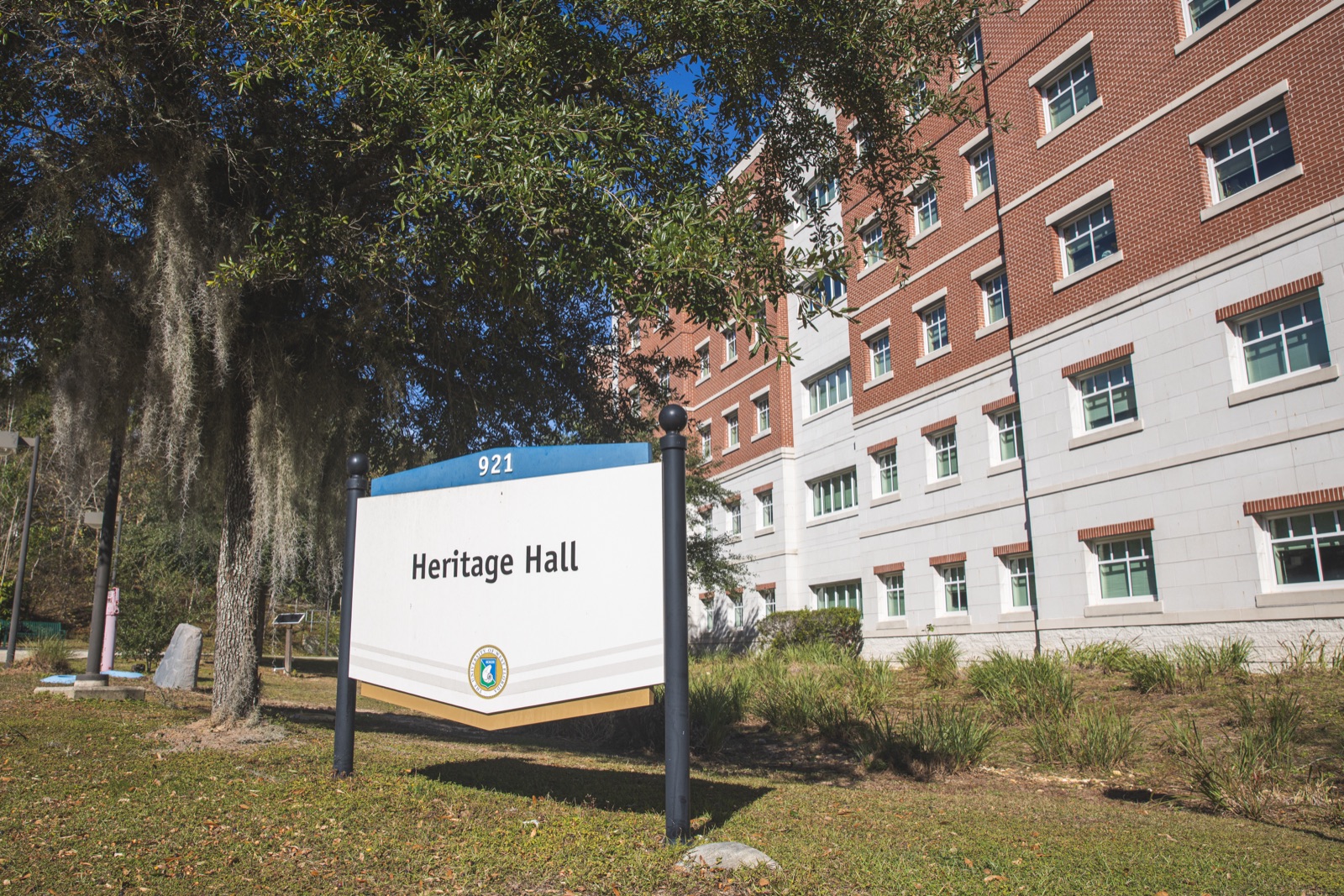 Heritage Hall sign in front of UWF's brick residence hall, with oaks draped in Spanish moss