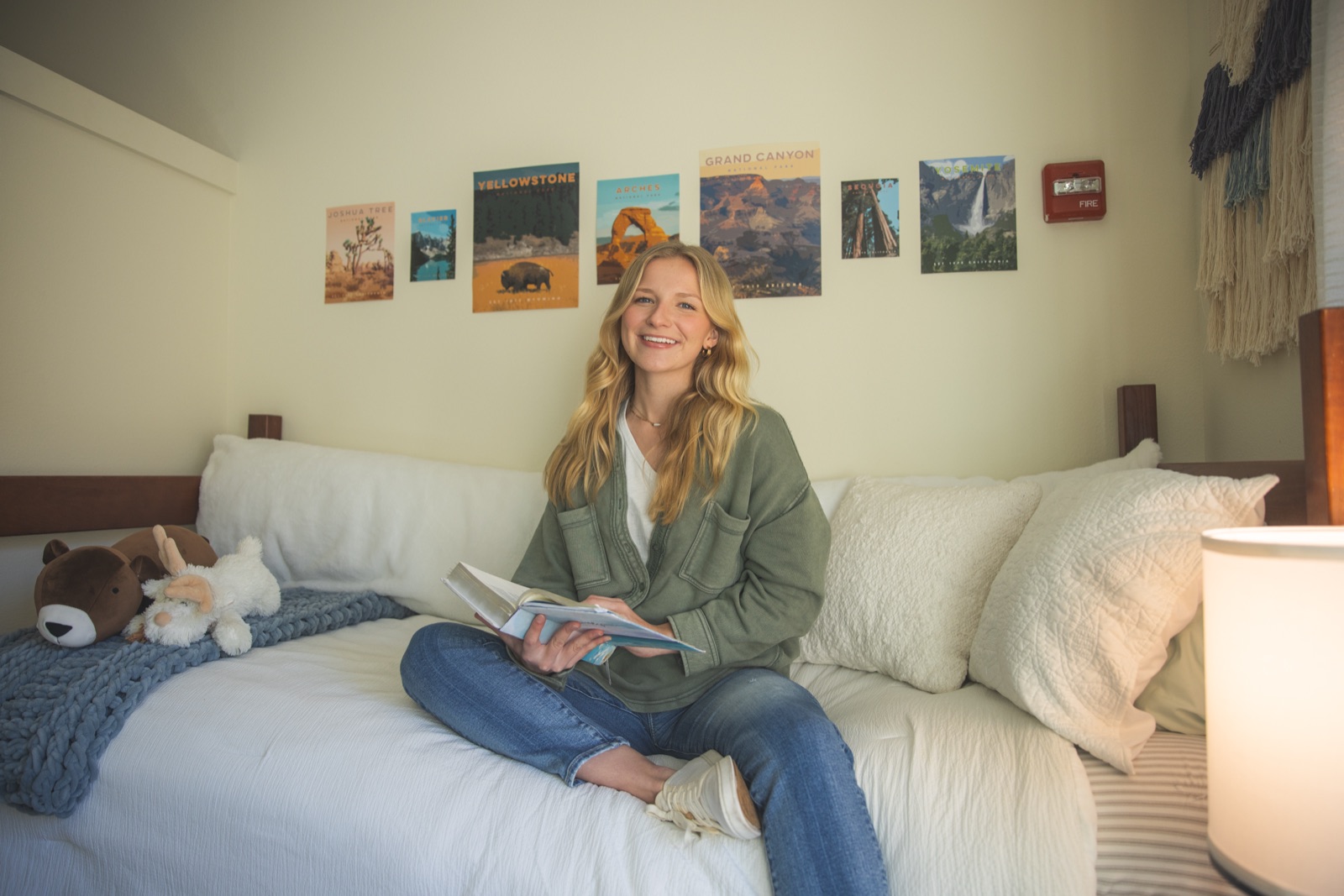 Student sitting on the bed in a Heritage Hall room, a UWF residence hall, with national-park posters on the wall