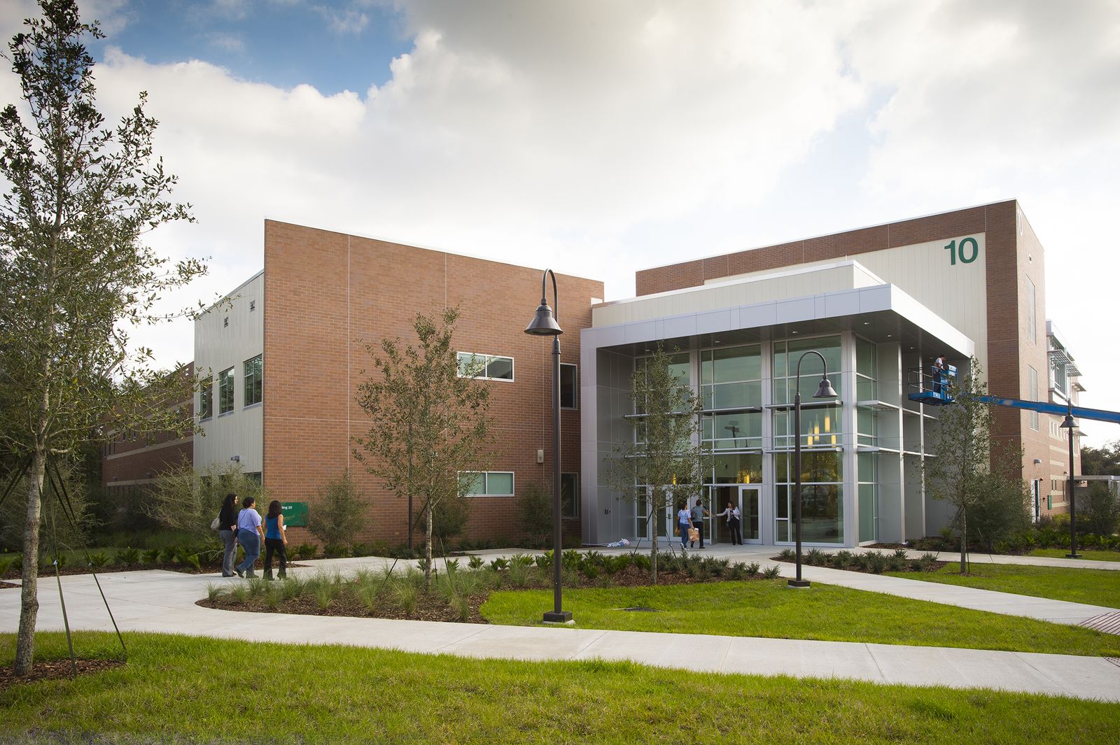 Fachada do Building 10, prédio de tijolos e vidro do West Campus da Valencia College em Orlando, com estudantes caminhando pela calçada em um dia de sol