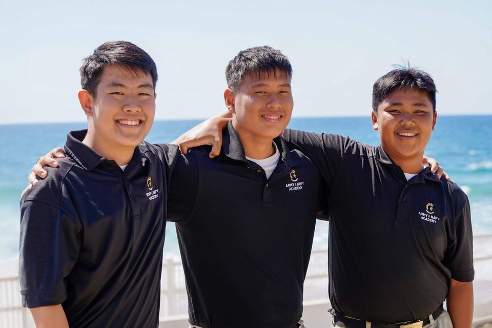 Três cadetes internacionais sorrindo juntos na praia