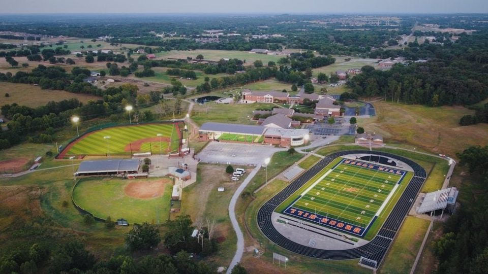 Vista aérea do complexo esportivo: estádio de futebol americano, pista de atletismo e campos de beisebol ao entardecer