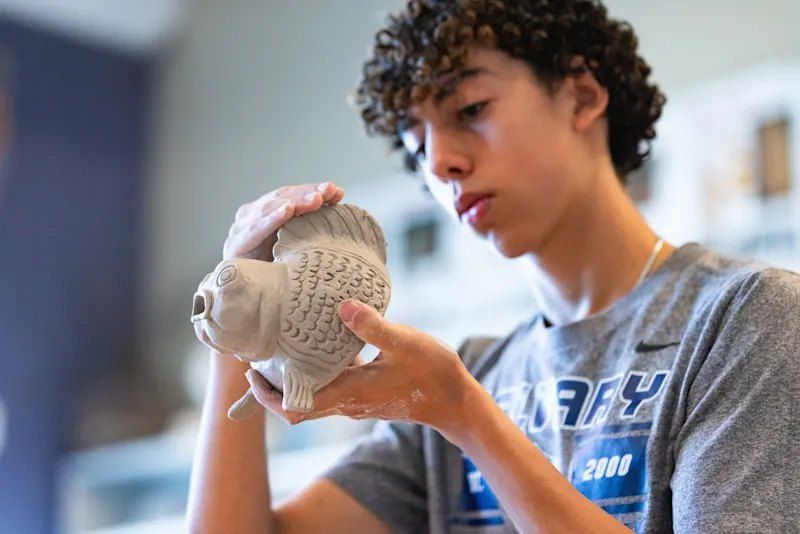 Aluno de camiseta da CCA observando uma escultura de peixe em argila na aula de arte