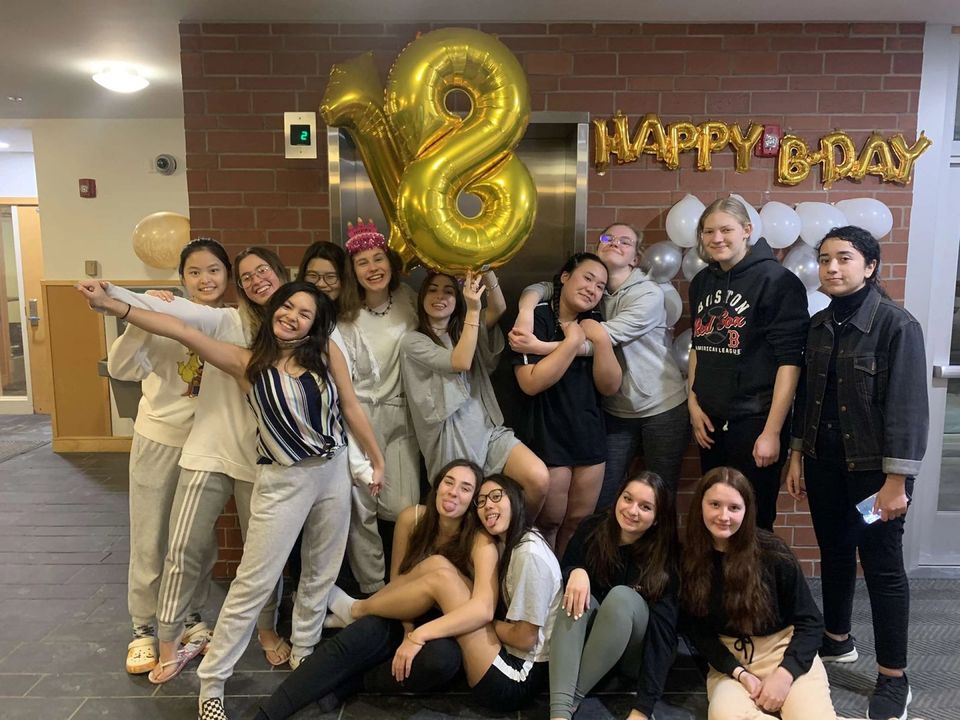 Grupo de alunas comemorando um aniversário de 18 anos no corredor do alojamento, com balões