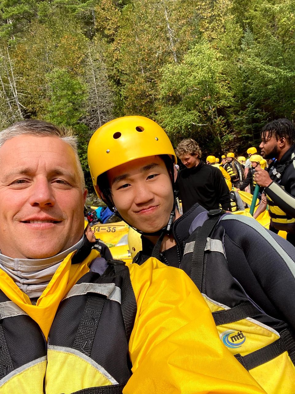 Aluno de capacete e colete ao lado de um professor em passeio de rafting