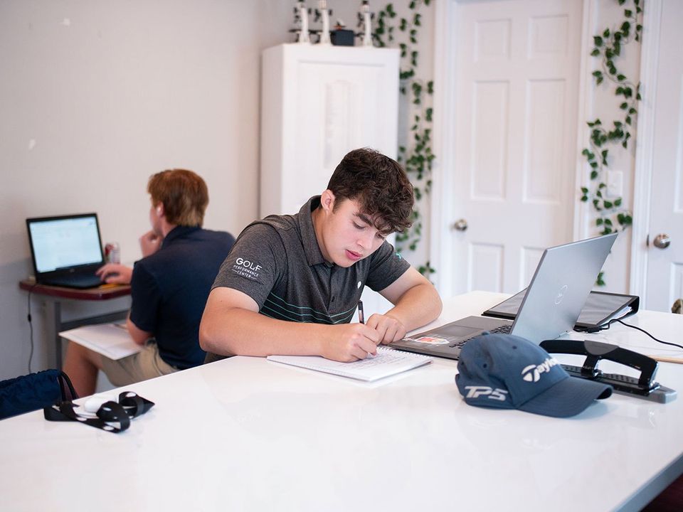 Aluno de polo do Golf Performance Center fazendo anotações ao lado do laptop na sala de estudos da academia