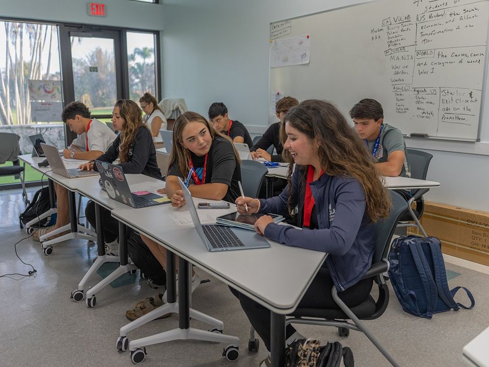 Alunos da academia com laptops e tablets em sala de aula, com palmeiras do lado de fora (campus da Flórida)