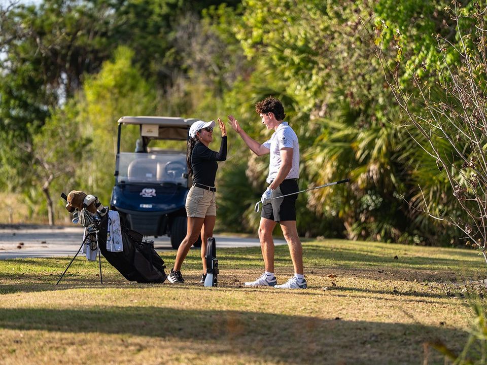 Técnica Natalia Quintero cumprimentando com high five um jovem golfista ao lado de um carrinho no campo