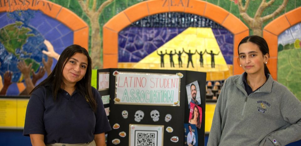 Dois alunos no estande da Latino Student Association, diante de um mural
