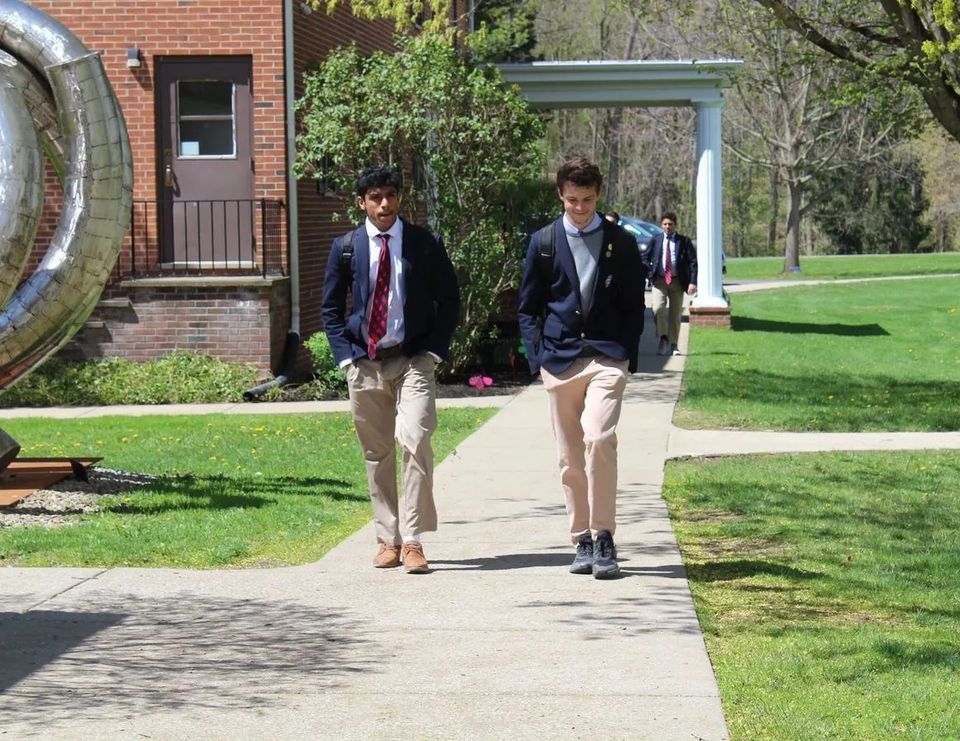 Alunos de blazer caminhando pela calçada do campus em frente a um prédio de tijolos