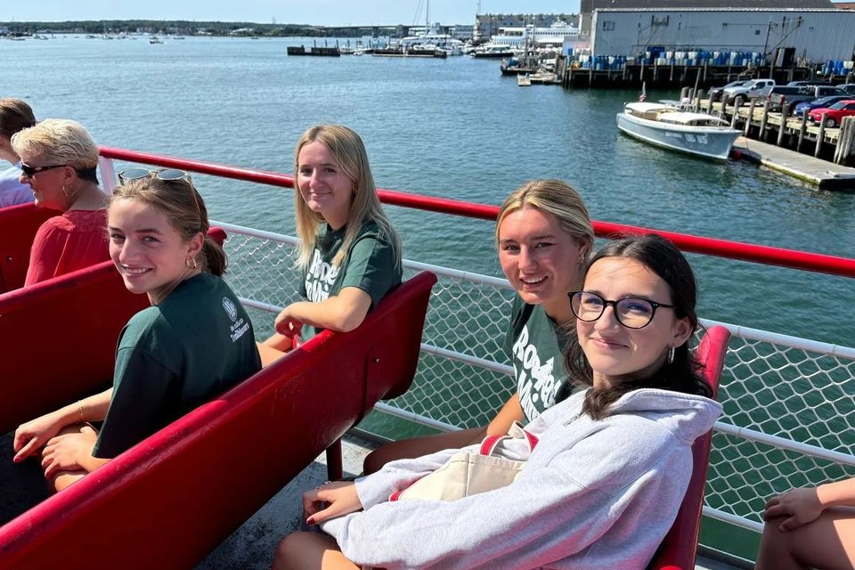Alunas sentadas no convés de um barco durante passeio em um porto