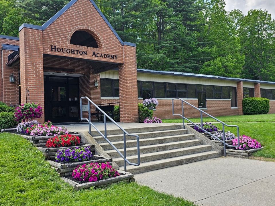 Entrada principal da Houghton Academy, prédio de tijolos com canteiros de flores