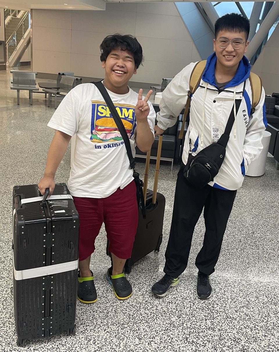 Dois alunos internacionais sorrindo com malas no saguão do aeroporto