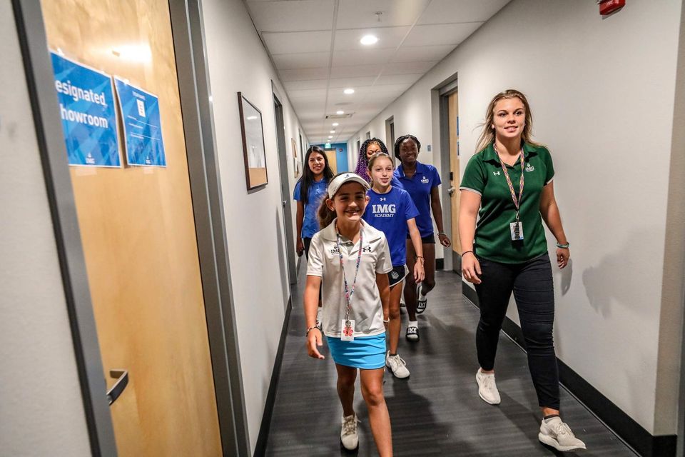 Mentora residencial caminhando com um grupo de meninas de polo da IMG por um corredor do dormitório