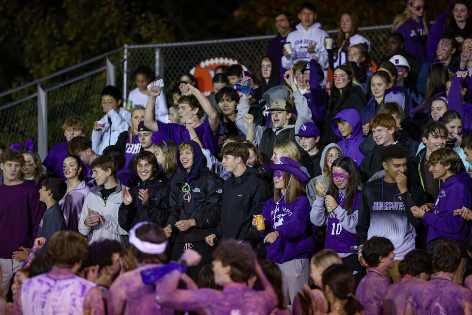 Torcida de alunos vestidos de roxo em um jogo noturno de futebol americano