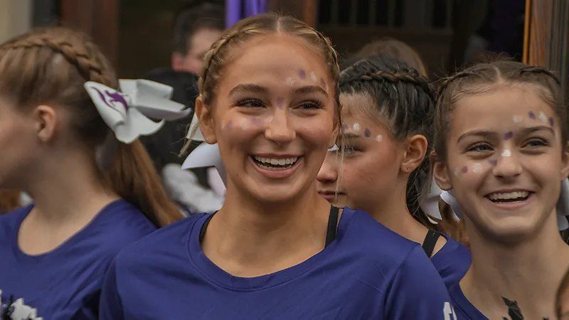 Alunas de camiseta roxa sorrindo com pintura no rosto em evento da escola