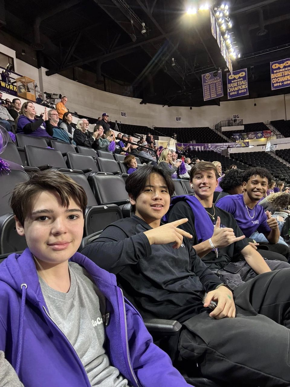 Quatro alunos internos sentados na arquibancada em um jogo de basquete universitário
