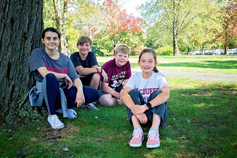 Quatro alunos do Middle School sentados na grama sob uma árvore no outono
