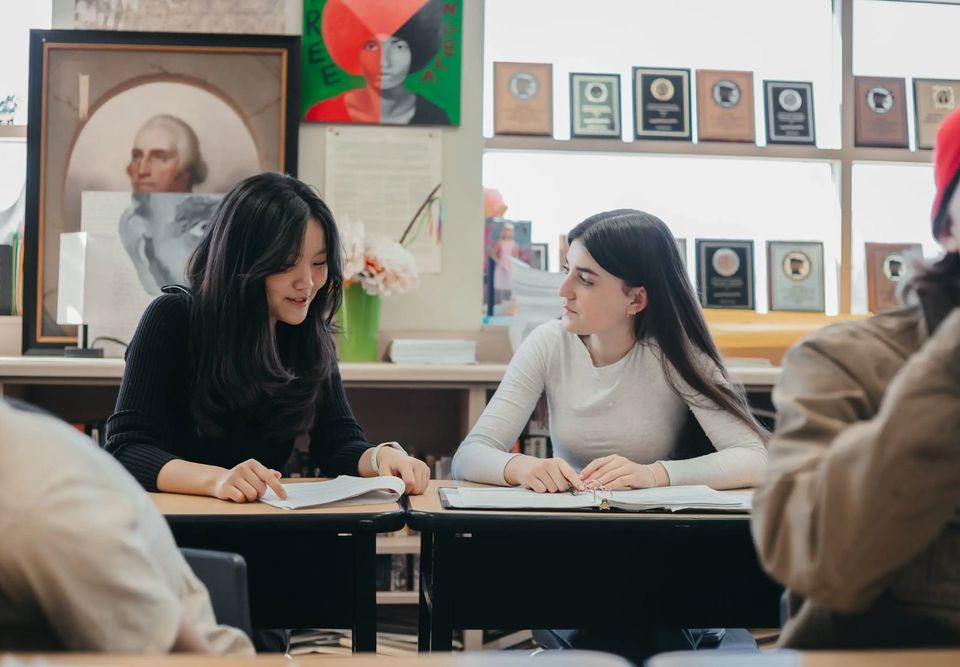 Dois alunos do Upper School discutindo a matéria em suas carteiras em uma sala de história