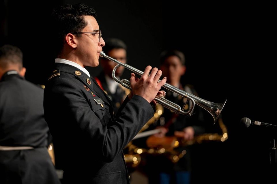 Cadete em uniforme de gala tocando trompete com a banda do NMMI no palco
